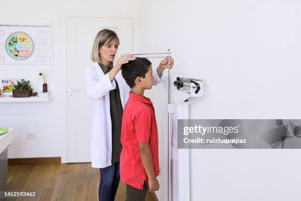 doctora nutricionista midiendo la altura y el peso de un niño pequeño en su consultorio médico - instrumento-de-medida fotografías e imágenes de stock