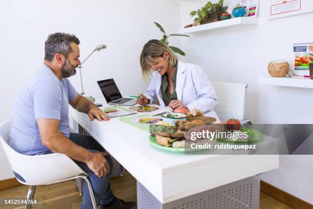 female nutricionist doctor in her office during a medical consultation with and overweight male patient - nutritionist stock pictures, royalty-free photos & images