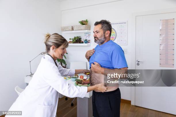 female nutricionist doctor in her office in a medical consultation mesuring corporal body mass index and waist contour with a mesuring tape off an overweight  male patient - body mass index chart stock pictures, royalty-free photos & images