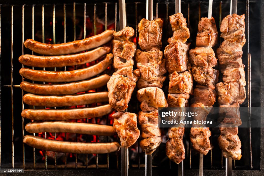 Meat on skewers and sausages are cooking on the grill. Concept of country picnic. Photography from above
