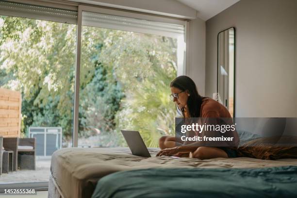 woman sitting on bed and using laptop at home in the morning - media day stockfoto's en -beelden