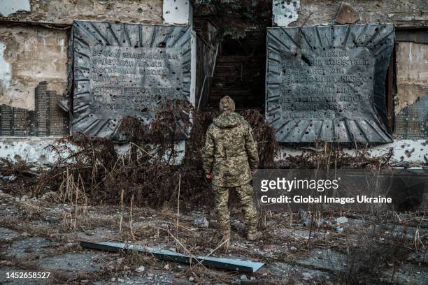 Ukrainian military member stands amid rubble in front of damaged by shelling Memorial to the Soviet soldiers who died during WWII on December 25,...