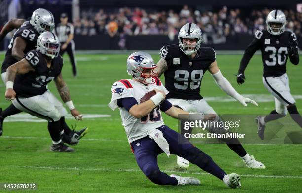 Quarterback Mac Jones of the New England Patriots slides in front of defensive end Maxx Crosby and safety Duron Harmon of the Las Vegas Raiders in...