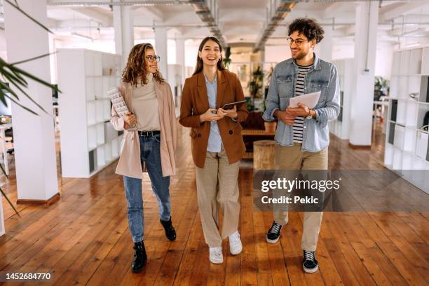 grupo de jóvenes colegas sonrientes caminando y hablando en una oficina moderna - aprendiz fotografías e imágenes de stock