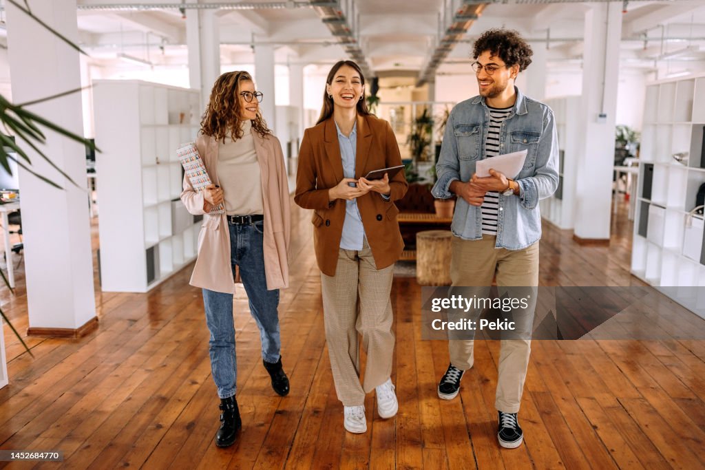 Group of smiling young colleagues walking and talking in modern office