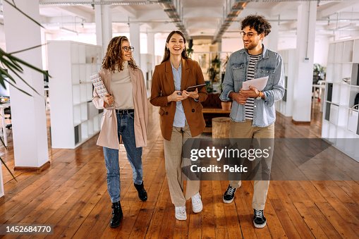Group of smiling young colleagues walking and talking in modern office Group of smiling young colleagues walking and talking in modern office