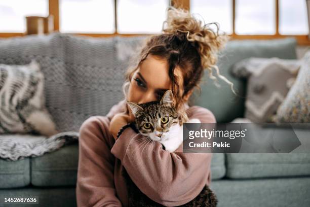 young woman bonding with her cat in apartment - people hugging imagens e fotografias de stock