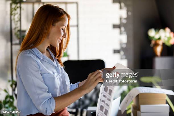businesswoman peeling off a shipping label, about to apply it on the package - etiketteren stockfoto's en -beelden