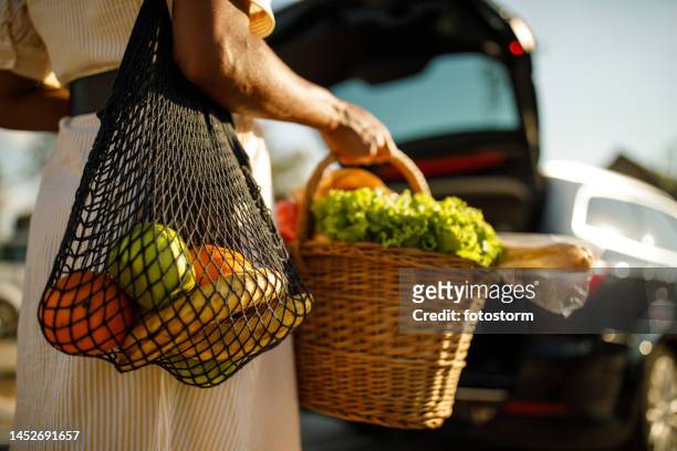 mujer cargando comestibles hacia su automóvil, que está a punto de cargar en el maletero - mercado de productos de granja fotografías e imágenes de stock