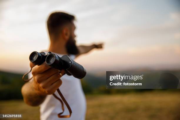 man giving you binoculars and pointing in the distance to where to look - verrekijker stockfoto's en -beelden