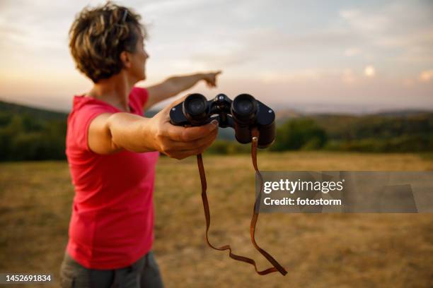 woman giving you binoculars and pointing to where to look at in the distance - breakthrough stock pictures, royalty-free photos & images