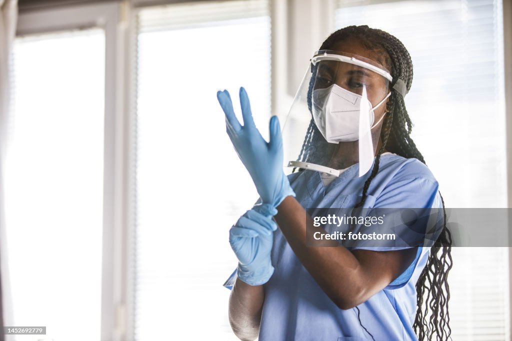Young nurse putting on disposable protective gloves before examining a patient