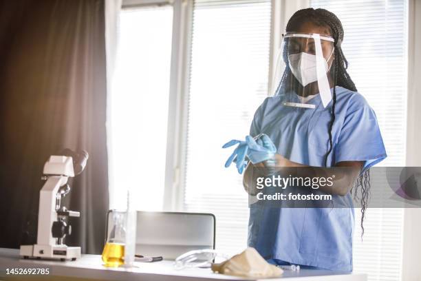 young nurse putting on disposable protective gloves before examining a patient - black glove stock pictures, royalty-free photos & images