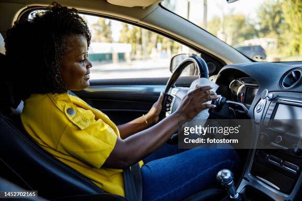 young woman cleaning the steering wheel in her car with antibacterial wet wipe - hand sanitizer in car stock pictures, royalty-free photos & images