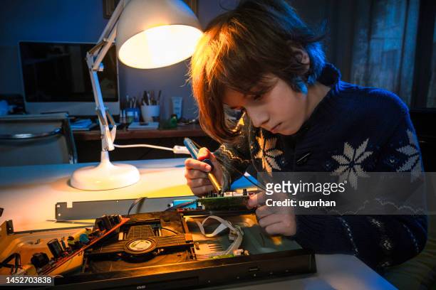 un pequeño niño genio está arreglando un dispositivo electrónico. - estudiando flexo fotografías e imágenes de stock