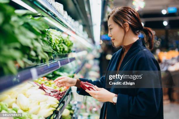 young asian woman grocery shopping in supermarket, choosing fresh organic fruits and vegetables along the produce aisle. fruits and vegetables shopping. routine shopping. zero waste. healthy eating diet and go green lifestyle - homegrown produce foto e immagini stock