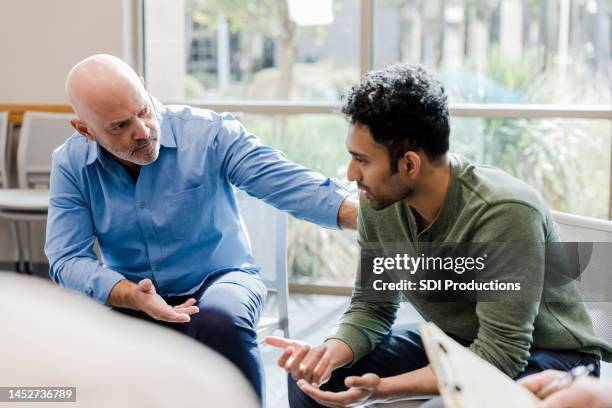 mature man helps younger man verbalize problems in therapy - man talking stock pictures, royalty-free photos & images