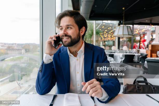 portrait of hispanic businessman talking with phone on restaurant window indoors - man suit using phone tablet foto e immagini stock
