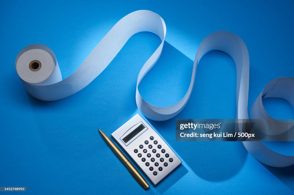 Adding machine tape and silver calculator against blue background,Malaysia