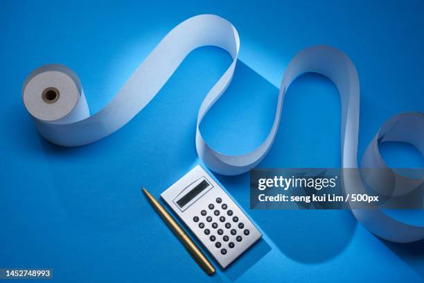 adding machine tape and silver calculator against blue background,malaysia - adding machine tape stock pictures, royalty-free photos & images