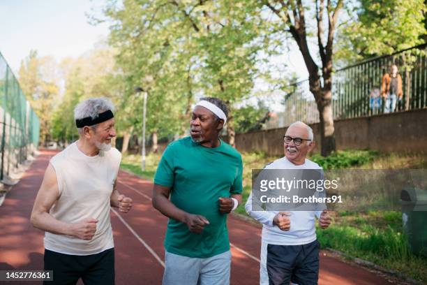 multirassische ältere männliche freunde, die zusammen auf der übungsbahn laufen - 3 old men jogging stock-fotos und bilder