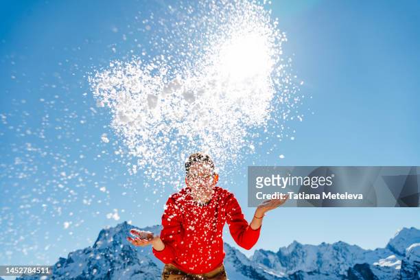 throwing snow in the mountain air. woman in red sweater throwing snow pile, wave in the air, standing in mountain area in sunny day - impact summit stock pictures, royalty-free photos & images