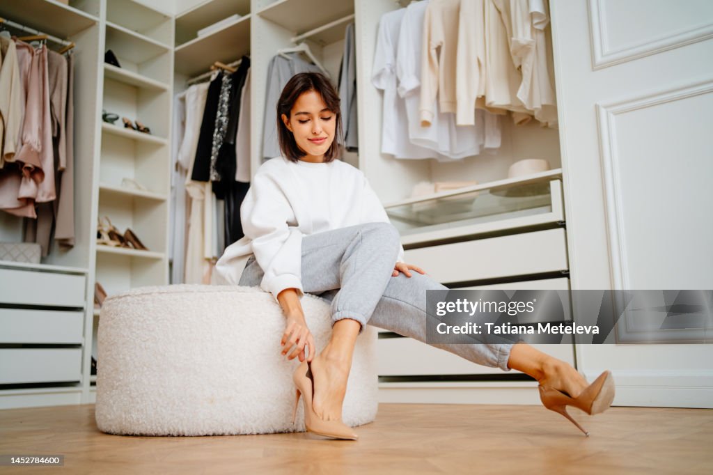 Posh brunette woman putting high heels shoes on soft stool in the closet of the store