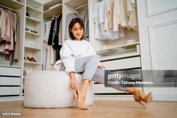 posh brunette woman putting high heels shoes on soft stool in the closet of the store - women trying on shoes - fotografias e filmes do acervo