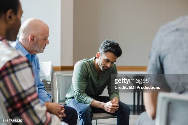 in group therapy, young man looks down while gathering thoughts - rehabilitate stock pictures, royalty-free photos & images