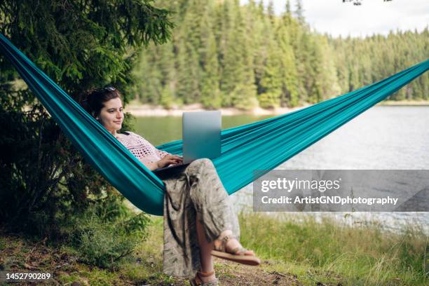 young woman lying in hammock using a laptop on a vacation. - hammock stockfoto's en -beelden