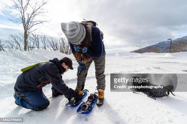 mountain guide helping to put snow shoes on student - snowshoe stock pictures, royalty-free photos & images