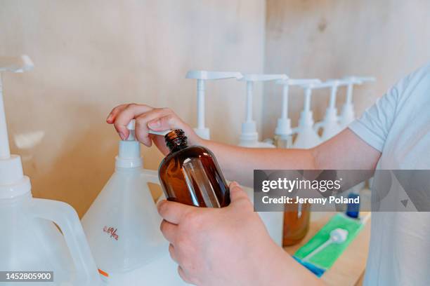 le mani della giovane donna pompano shampoo o bagnoschiuma da una bottiglia, facendo scelte sostenibili in un negozio al dettaglio senza plastica - ricaricare foto e immagini stock