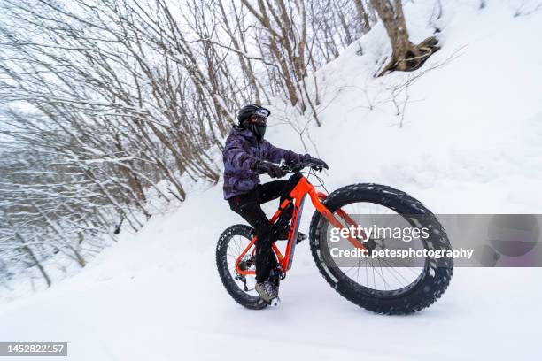 a man riding a mountain bike with large fat tires down a snowy forest mountain road - snow falls in wider area in japan imagens e fotografias de stock