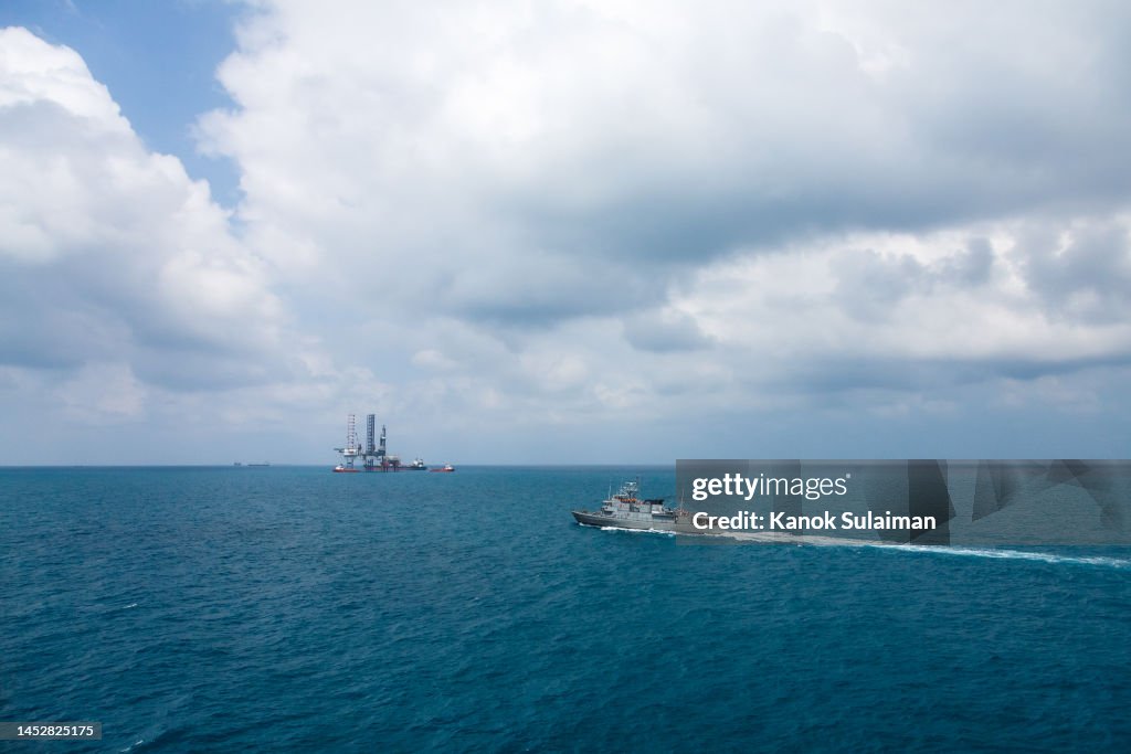 A warship is patrolling the sea with oil rig platform background view from aerial