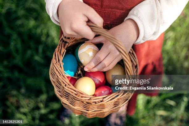 little girl hands holding multicolored easter eggs in the basket outdoors. - happy easter in russian stock-fotos und bilder