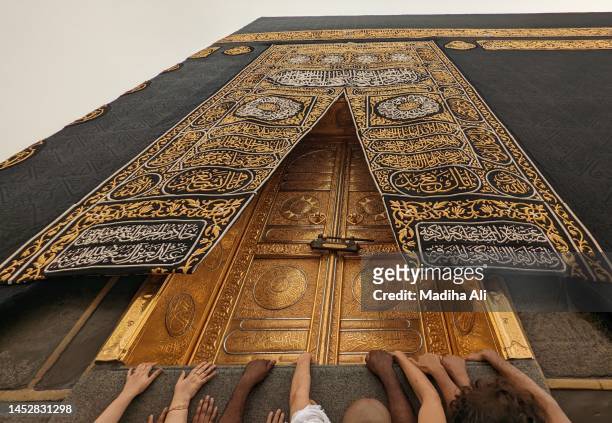 pilgrims touching kiswah cloth and gold door of khana kaba | people doing tawaaf and touch khaana kaaba in holy mosque of al haram for hajj and umrah | wearing ihram clothes for haj and umra, mecca, saudi arabia - kaba at mecca stock pictures, royalty-free photos & images
