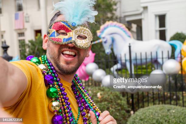 ein junger lateinamerikanischer tourist, der maske, kostüme und halsketten trägt, feiert mardi gras durch die straßen, während er ein selfie mit seinem handy in new orleans macht. - new orleans mardi gras stock-fotos und bilder