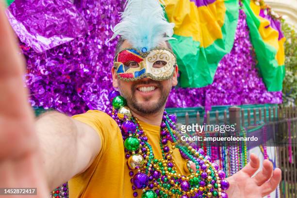 a young latin tourist male, wearing mask, costumes and necklaces celebrating mardi gras through the streets while taking a selfie with his cellphone in new orleans. - mardi gras float stock pictures, royalty-free photos & images