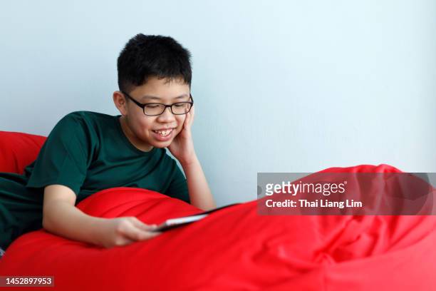 boy lying down on a bean bag and holding a book. children leisure reading concept - boy lying down stock pictures, royalty-free photos & images