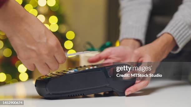 nahaufnahme der asiatischen frau kauf per kreditkarte auf elektronischen zahlungsautomaten oder kartenleser in einem kleinen laden in der weihnachtsnacht. - customers pay with contactless cards stock-fotos und bilder