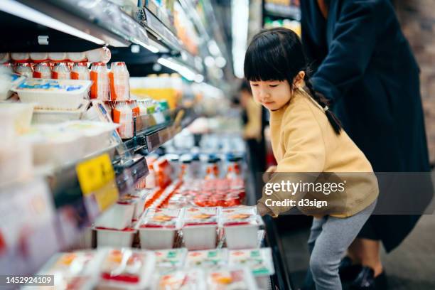 lovely little asian girl grocery shopping with her mother in supermarket, choosing dairy product on the shelf along the dairy aisle. routine grocery shopping. healthy eating lifestyle - mom buying milk stock-fotos und bilder