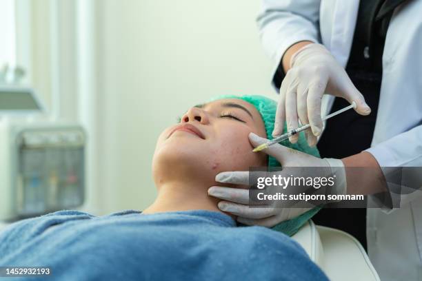 facial botox injection on the cheek of a young woman undergoing treatment in a beauty clinic - plastische chirurgie stockfoto's en -beelden