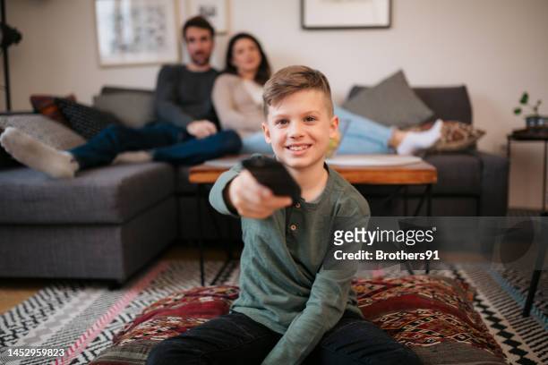 niño sonriente con control remoto viendo la televisión en casa - familia viendo tv fotografías e imágenes de stock