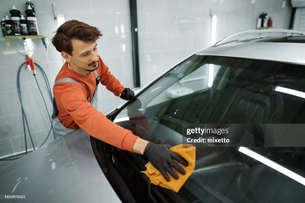 Professioneller Auto-Detailierer wischt Auto-Windschutzscheibe mit Mikrofaser-Handtuch in seiner Garage ab