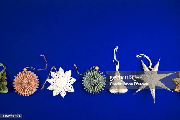 paper snowflakes and christmas tree ornaments in festive composition on blue background. merry christmas and a happy new year concept pattern - paper snowflakes stock-fotos und bilder