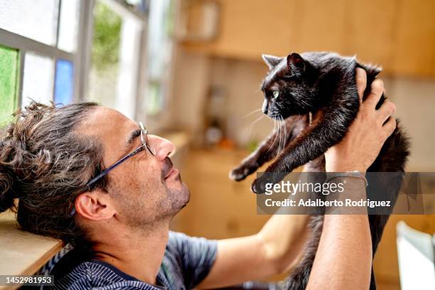man lifting black cat in arms - black and white cat foto e immagini stock