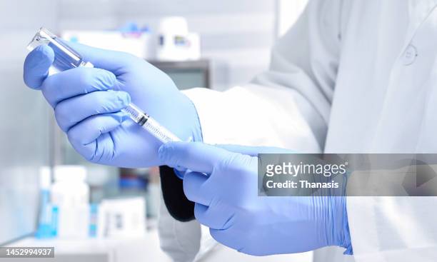 close-up on man hands , wearing protective gloves, dialing medicine into syringe from a vaccine vial - dose fotografías e imágenes de stock