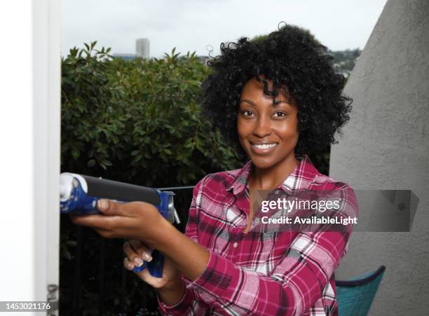 african american caulking gun woman smiles at camera horizontal - caulk gun stock pictures, royalty-free photos & images