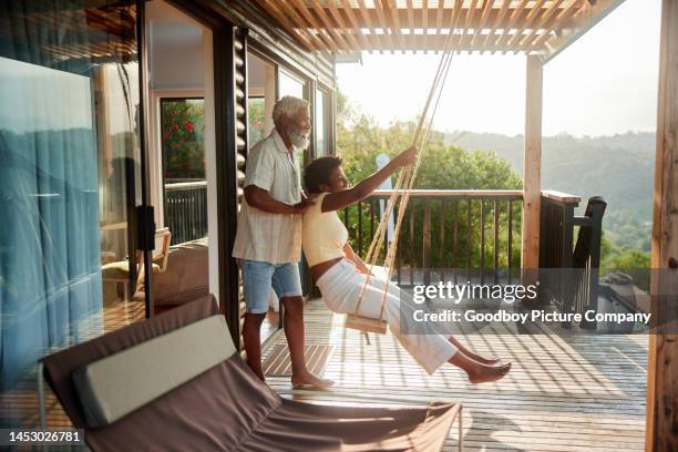 man pushing his wife on a swing on the balcony with a scenic view - couple swinging stock pictures, royalty-free photos & images