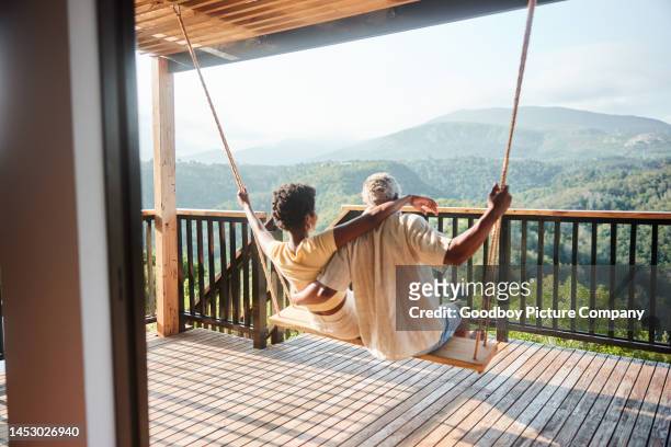couple sitting on a balcony swing and looking out at the scenic view - mature adult couple stockfoto's en -beelden